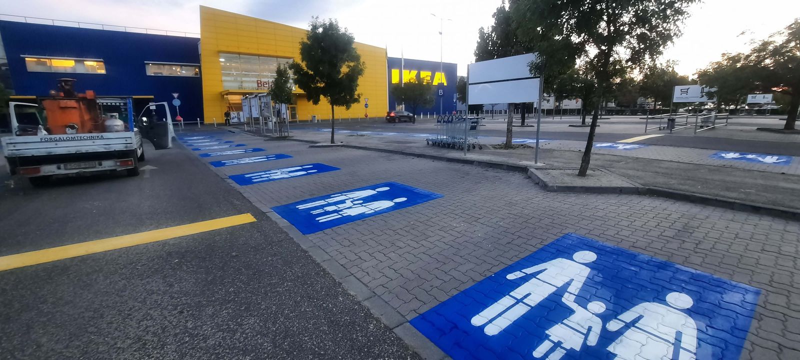 Kék alapú családi parkolóhely-jelek felfestése egy áruház parkolójában
